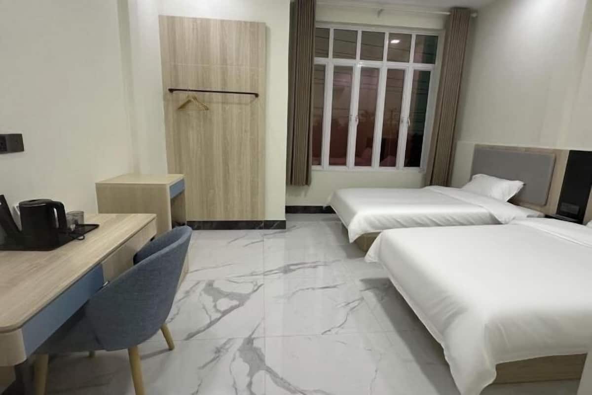 A hotel room with a desk, two beds, a chair, a wardrobe, and a window.