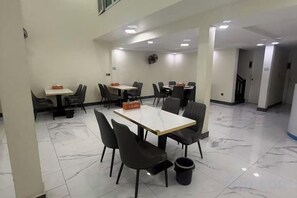Ein Speisesaal eines Hotels mit Tischen, Stühlen, einem Papierkorb und einer Uhr an der Wand.