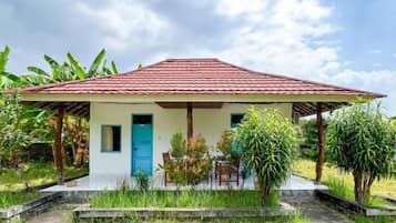 A single-story house with a red-tiled roof, a blue door, and a small porch with a chair.