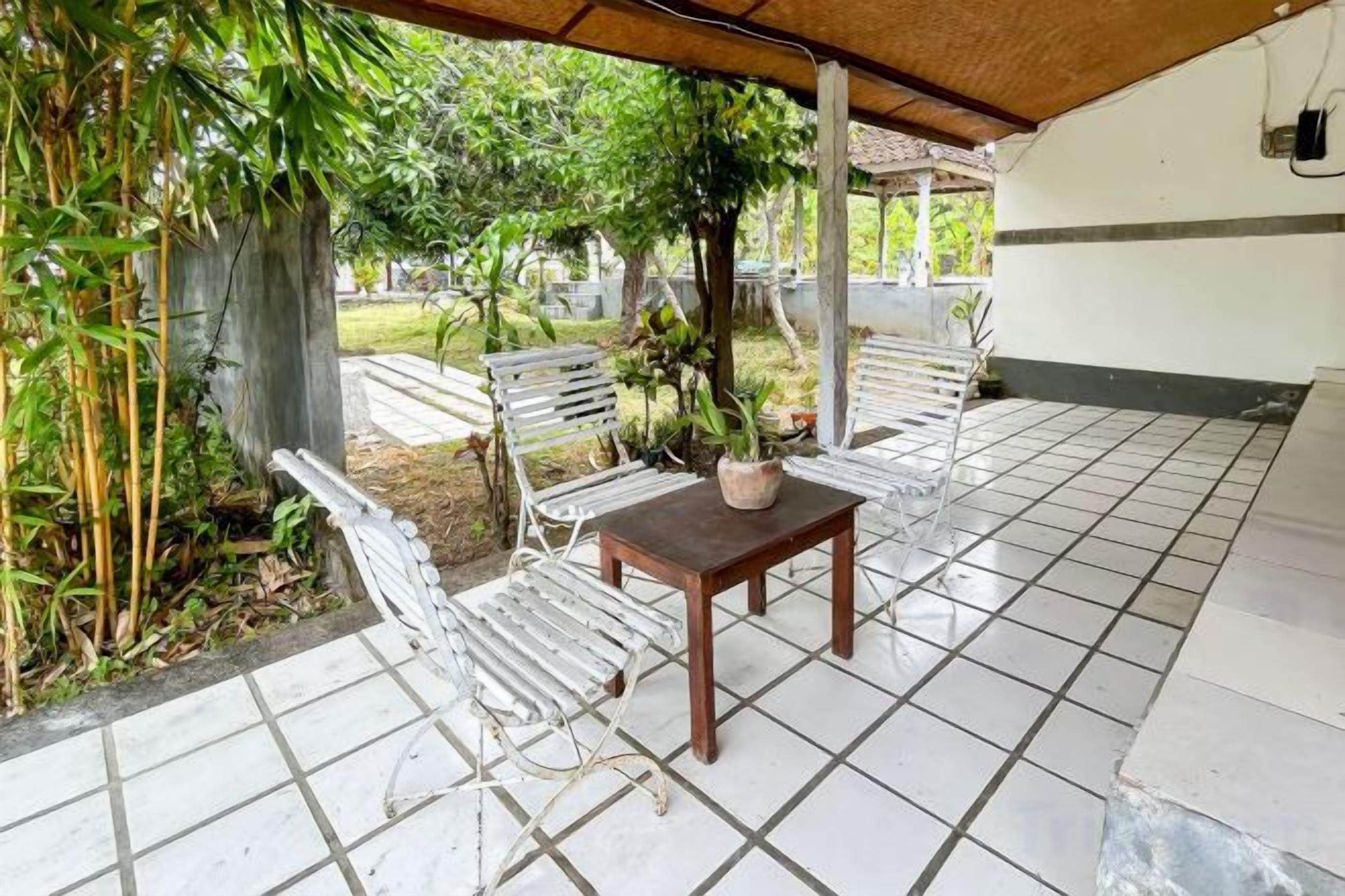 An outdoor patio with tiled flooring, white metal chairs, a wooden table, and a potted plant.