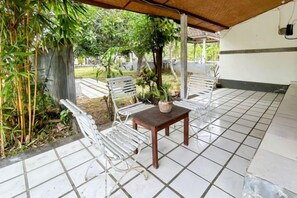 An outdoor patio with tiled flooring, white metal chairs, a wooden table, and a potted plant. - Hepi Bungalow Lovina Mitra RedDoorz (Bali)