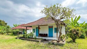 A single-story building with a red-tiled roof, a porch with seating, and a small tree in front. - Hepi Bungalow Lovina Mitra RedDoorz (Bali)
