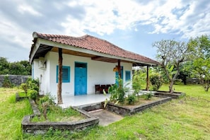 A single-story house with a red-tiled roof, a blue door, and a small porch area. - Hepi Bungalow Lovina Mitra RedDoorz (Bali)