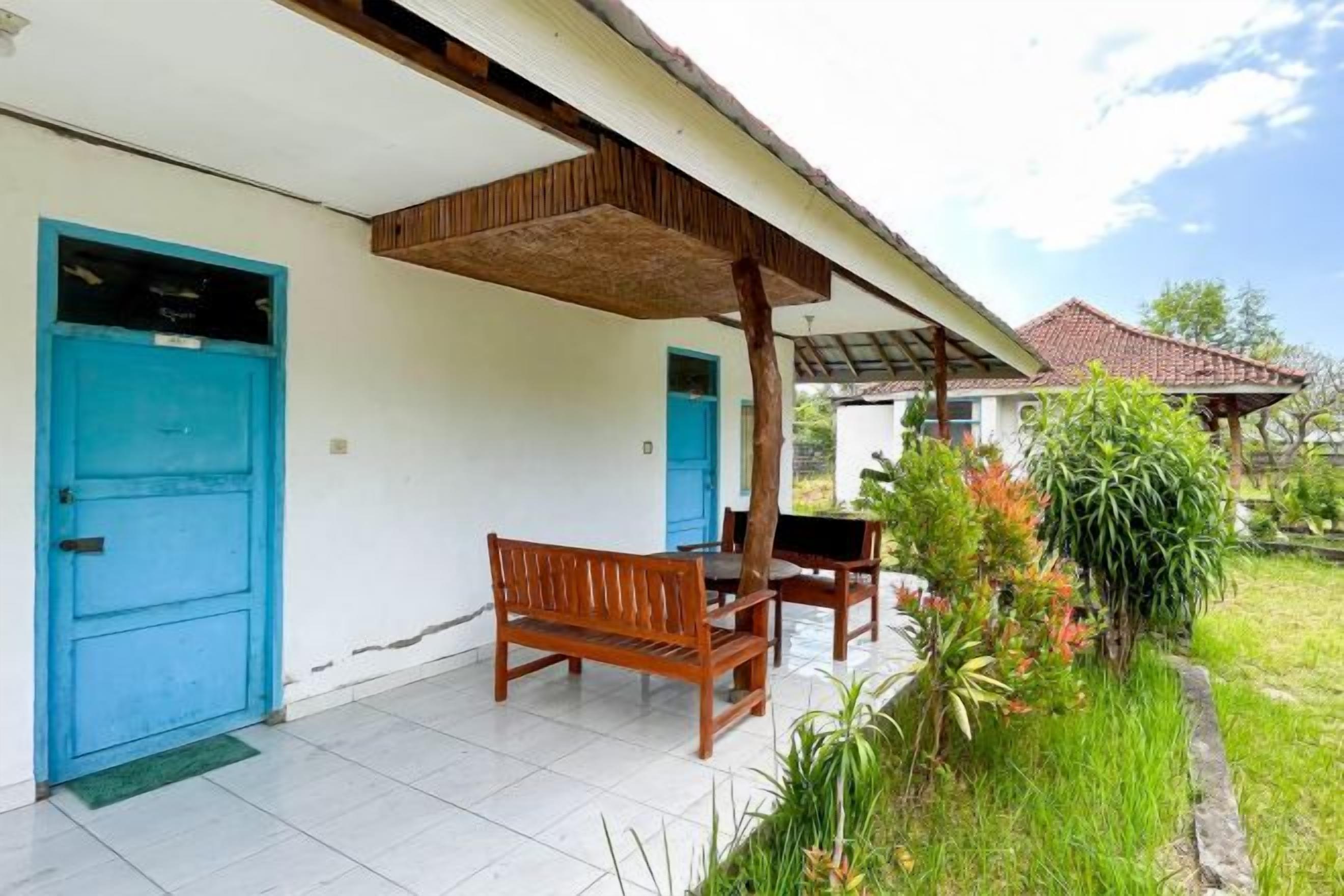 A covered outdoor seating area with a bench and table, a blue door, and a garden with various plants.