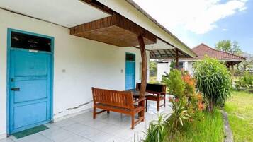 A covered outdoor seating area with a bench and table, a blue door, and a garden with various plants.
