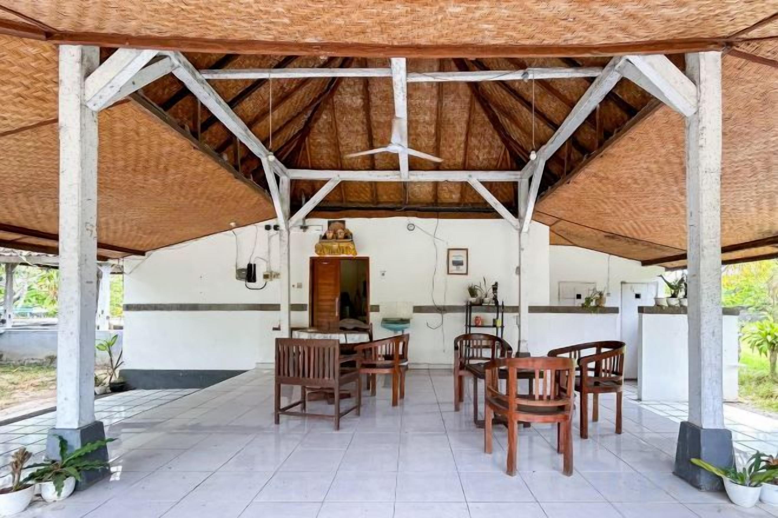A covered outdoor dining area with a table and chairs, a kitchen in the background, and a thatched roof.