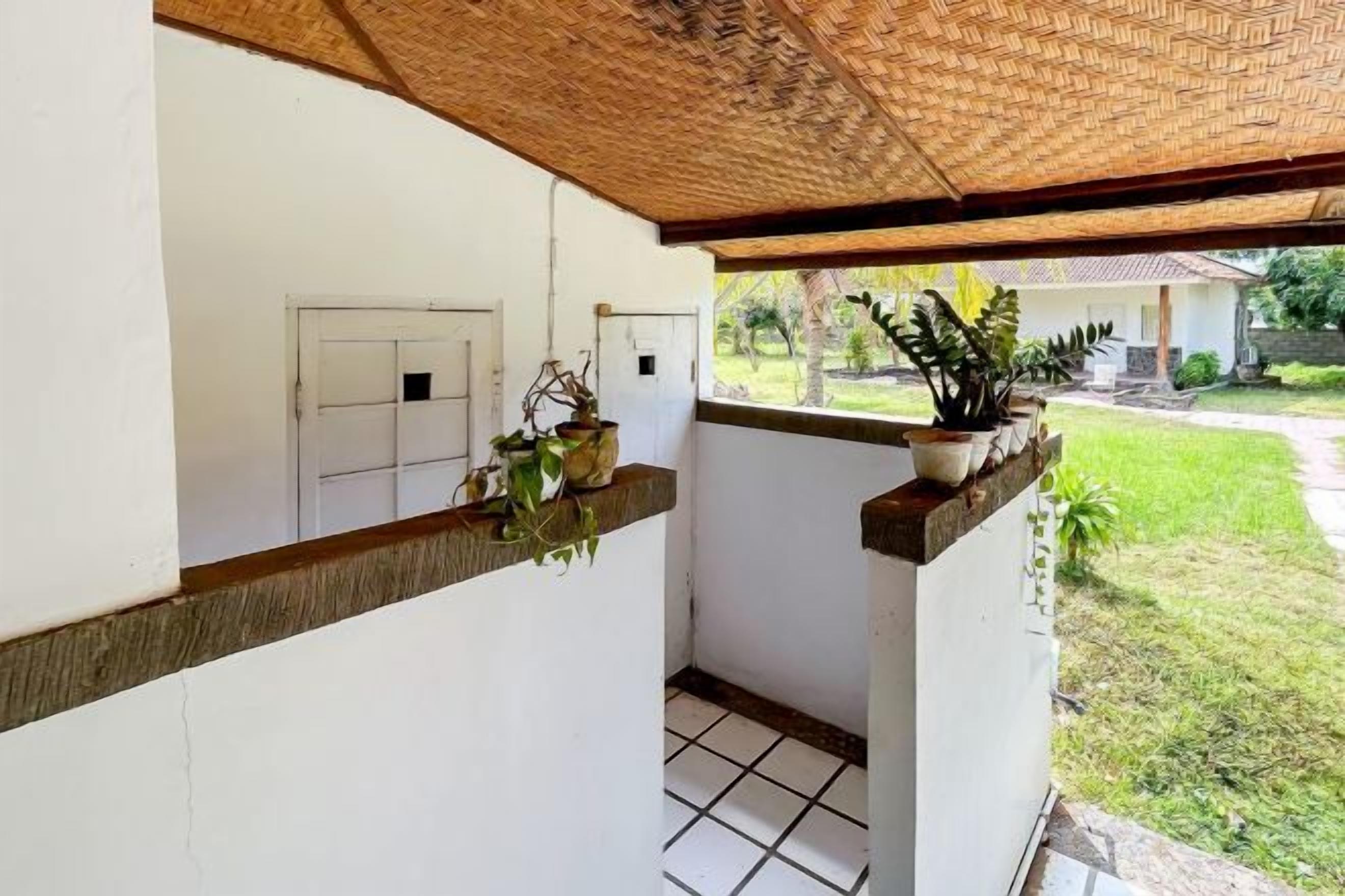 A covered balcony with potted plants, a tiled floor, and a view of a house and garden.