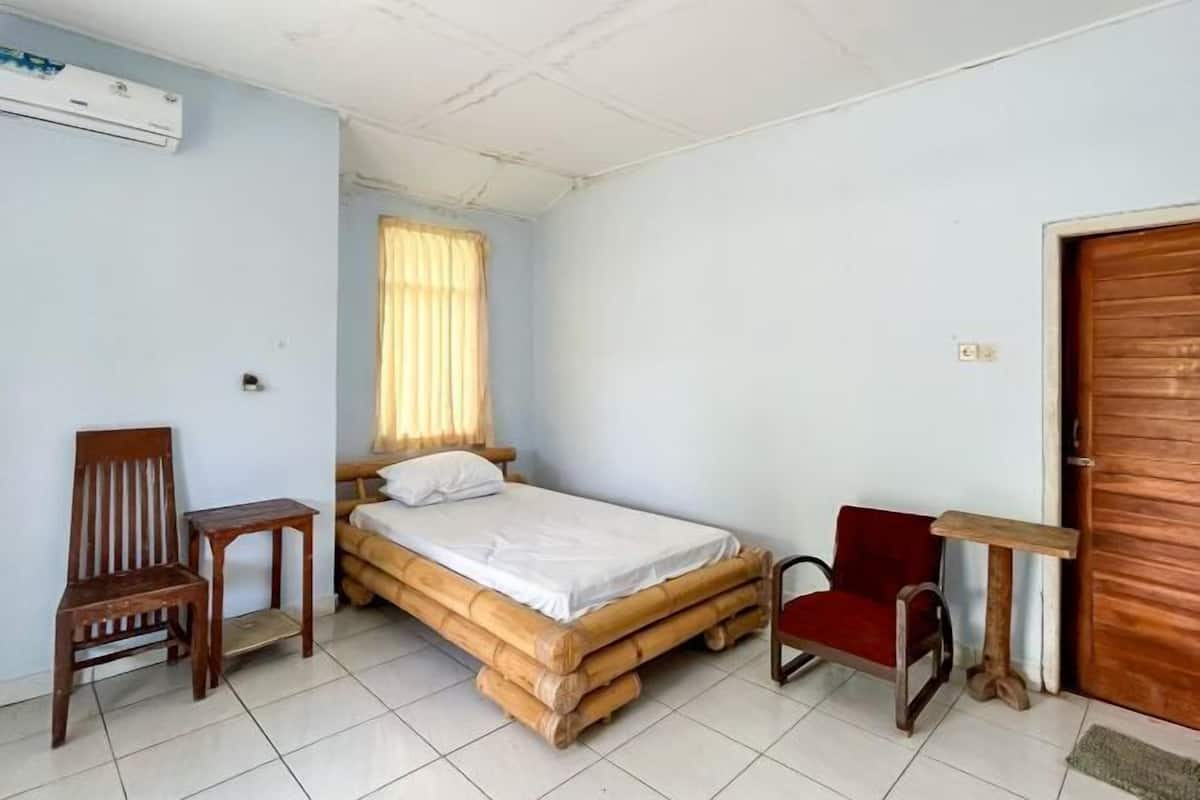 A room with a bed, two chairs, a small table, and a wooden door.