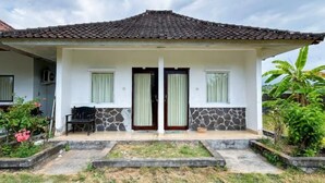 A two-story house with a tiled roof, a front porch, and a small garden area. - Hepi Bungalow Lovina Mitra RedDoorz (Bali)