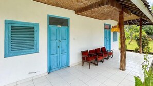 A covered outdoor seating area with a white wall, blue doors, and red chairs.