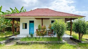 A single-story house with a red-tiled roof, a blue door, and a small porch with chairs and plants.