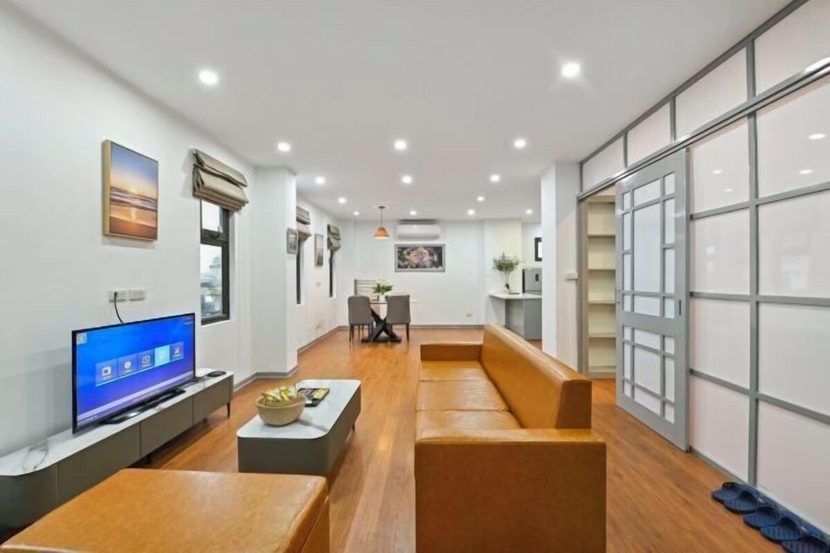 A modern living room with a sofa, a coffee table, a TV, and a dining area with chairs.
