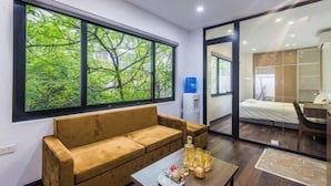A modern room with a large window, a sofa, a table with items, and a bed in the background. - 22HOUSING SERVICE APARTMENT (Hanoi)