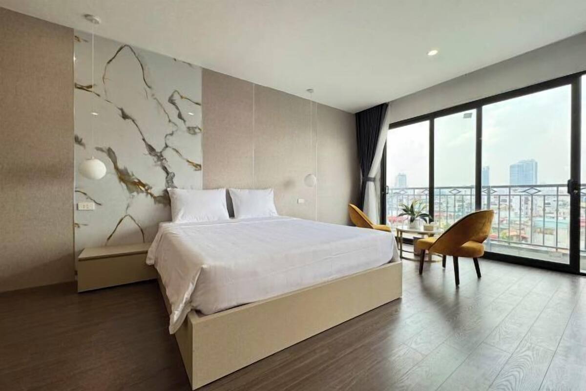 A modern hotel room with a large bed, a dining area, and a balcony with a city view.