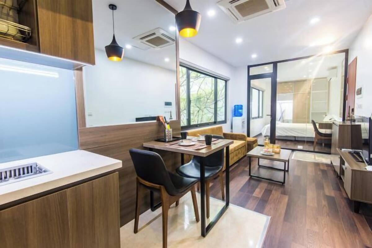 A modern hotel room with a dining area, a sofa, a bed, and a bathroom visible through a glass door.