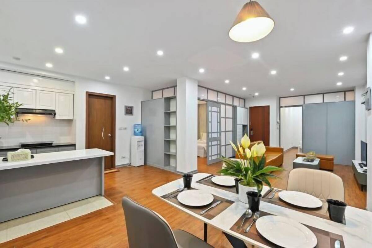 A modern kitchen with white cabinets, a wooden door, and a dining area with a table set for four.