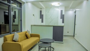 A modern hotel room with a sofa, two small tables, a marble wall, and a radiator. - Kigali Bliss Apartment (Kigali)