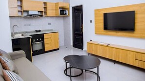 A modern kitchen with wooden cabinets, a built-in microwave, and a black stove. There's a TV mounted on the wall and a small round table in the living area. - Kigali Bliss Apartment (Kigali)