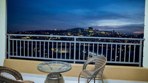 A balcony with wicker chairs and a glass table, overlooking a cityscape at night. - Kigali Bliss Apartment (Kigali)