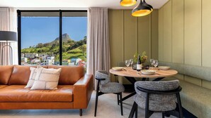 Ein modernes Wohnzimmer mit einer Ledersofa, einem Esstisch mit Stühlen und Blick auf eine Berglandschaft durch große Fenster.