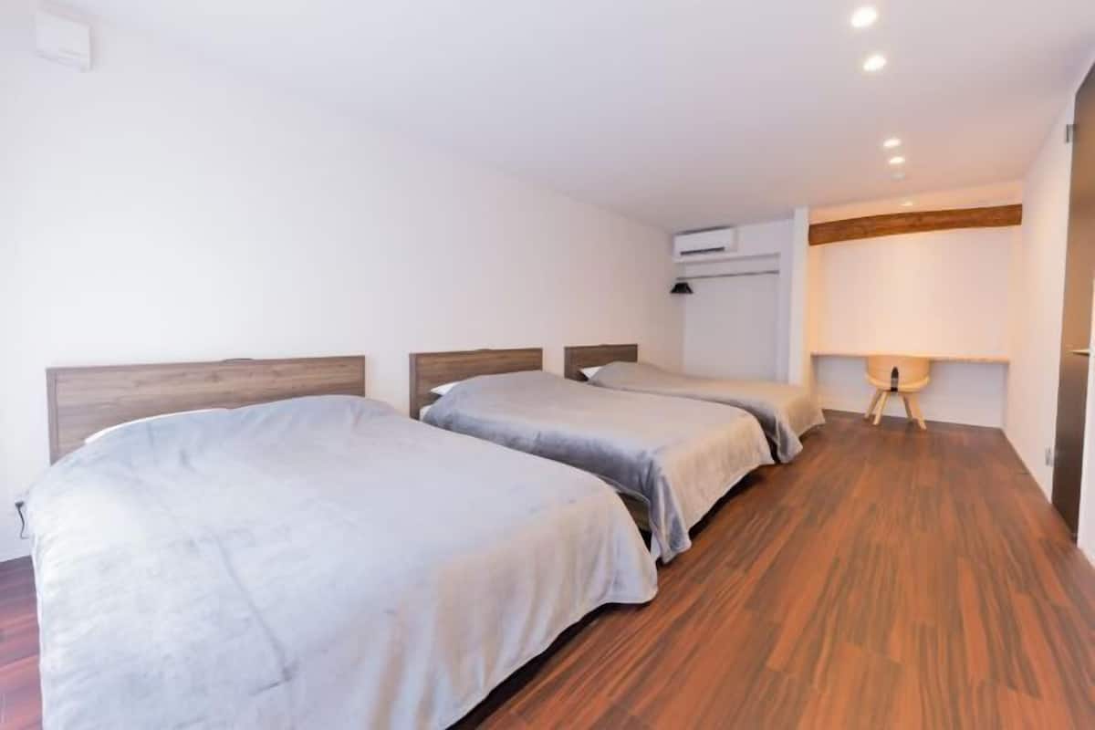 A hotel room with two single beds, wooden flooring, a wall-mounted air conditioner, and a bedside lamp.