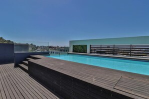 A rooftop swimming pool with a wooden deck and a view of the city skyline.