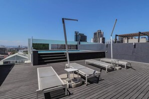 En tagterrasse med liggestole, en pool og en bysilhouet i baggrunden.