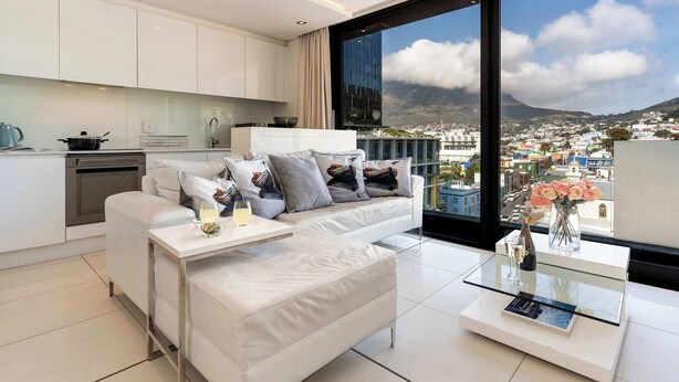 A modern living room with a white sofa, a glass coffee table, and a view of a cityscape through large windows.