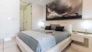 A modern bedroom with a large bed, bedside tables, and a painting of a cloudy sky.