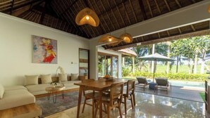 A spacious living area with a dining table, sofa, and a view of a pool and garden. - The Lanaya Villa (Bali)