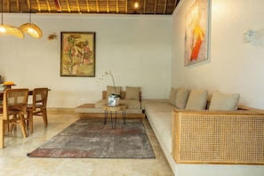 A living room with a sofa, a coffee table, and a dining area with chairs. - The Lanaya Villa (Bali)