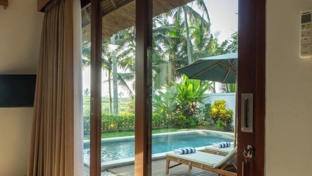 A room with a sliding glass door leading to a pool area with lounge chairs and an umbrella. - The Lanaya Villa (Bali)