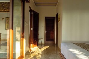 A hotel room with a bed, a small table, and a door leading to another room. - The Lanaya Villa (Bali)