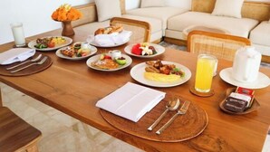 A breakfast setting with various dishes, a glass of orange juice, and a coffee maker on a wooden table. - The Lanaya Villa (Bali)