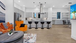 Een moderne keuken met een centraal eiland, barstoelen en een eethoek met een grijze bank en een oranje fauteuil.