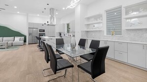 Een moderne keuken met een glazen eettafel, zwarte stoelen en witte kastjes.
