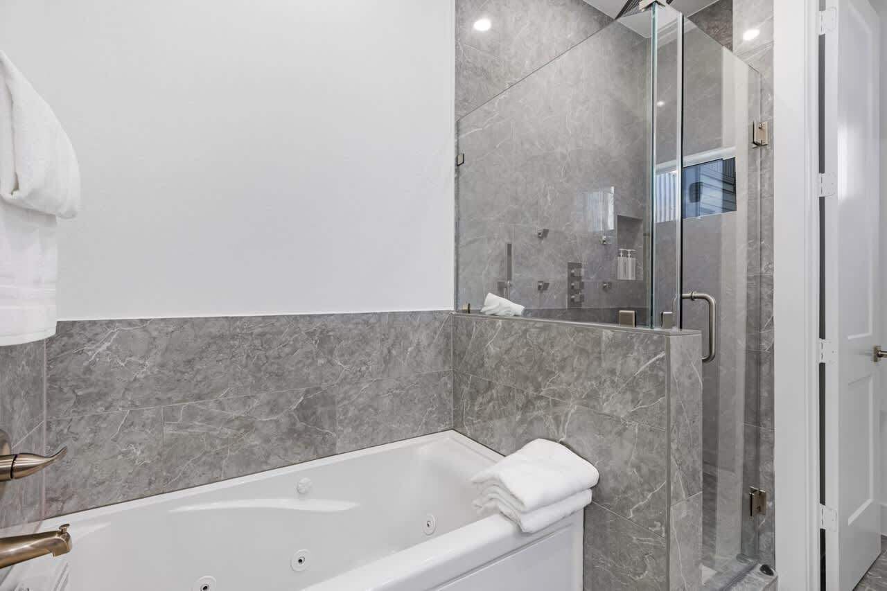 Ein modernes Badezimmer mit einer Badewanne, einer Duschkabine aus Glas und Marmorwänden.
