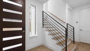Een modern interieur met een donkerhouten deur, een trap met zwarte leuningen en een lichtgekleurde vloer.