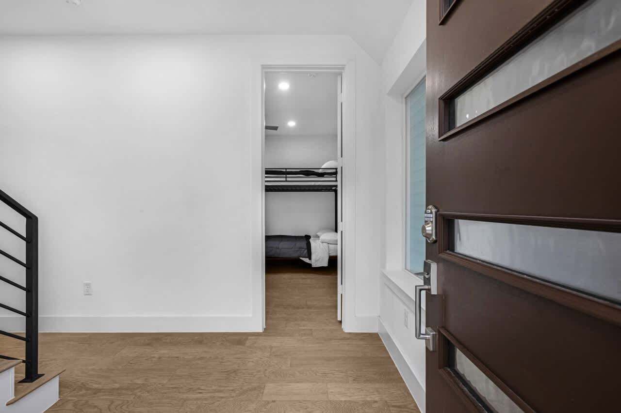 A hallway leading to a bedroom with a bunk bed, a wooden floor, and a brown door.