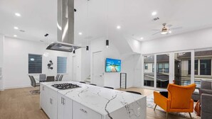 Een moderne keuken met een centraal kookeiland, een eethoek met oranje stoelen en een groot raam met uitzicht.