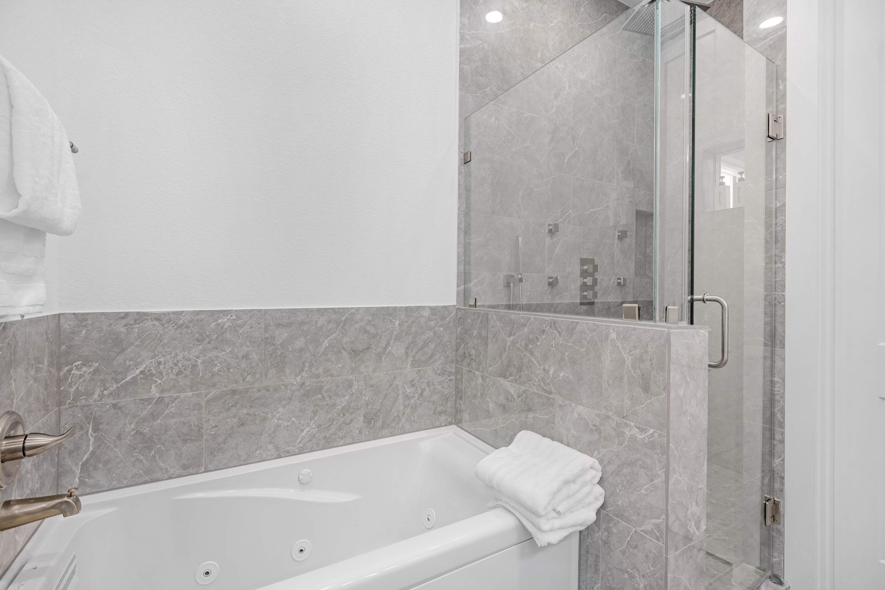A modern bathroom with a marble-tiled shower enclosure, a white bathtub, and a towel hanging on the wall.