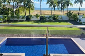 Una piscina con barandilla de vidrio, vista al océano y palmeras.