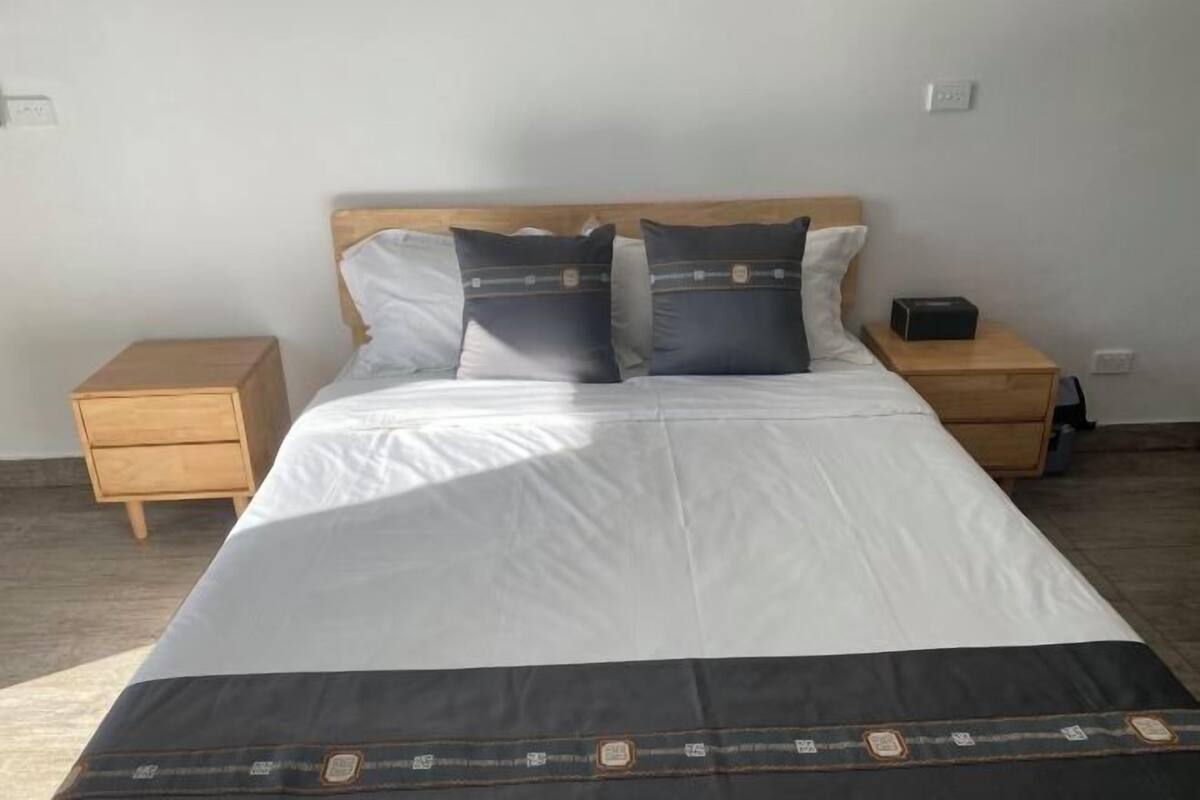 Uma cama com cabeceira de madeira, duas mesas de cabeceira e um abajur.