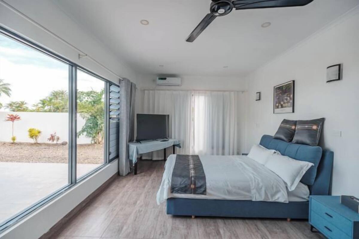 Quarto com cama, escrivaninha, televisão e ventoinha no teto.
