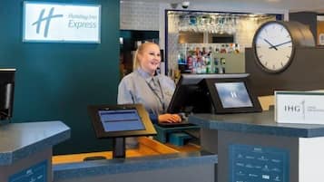 A Holiday Inn Express reception desk with a digital display, a clock, and a bar area in the background.