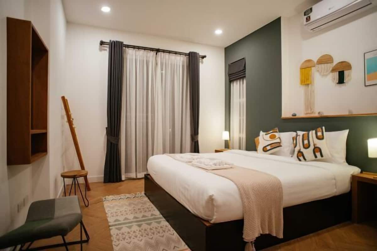 A bedroom with a bed, bedside tables, a chair, a window with curtains, and a wall-mounted air conditioner.