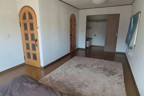 A room with a large rug, wooden doors, and a visible kitchen area in the background. - Cherry Blossom House (Saitama)