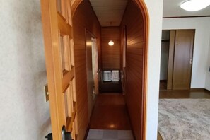 Un couloir aux murs recouverts de lambris en bois, une porte au fond et un luminaire au plafond.