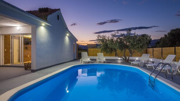 Una piscina con lettini, un ingresso con porta in vetro e vista sul tramonto.