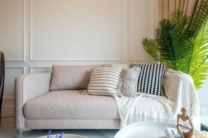Ein beiges Sofa mit gemusterten Kissen, einer weißen Decke und einem kleinen Tisch mit einer Vase und einer Figur.